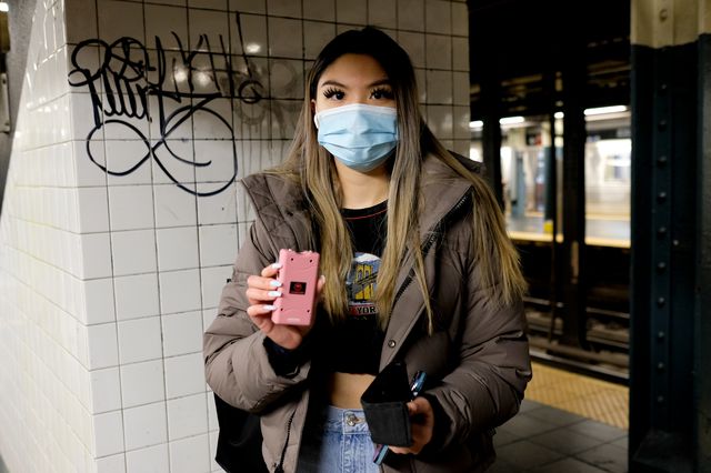 A young woman in a mask holding up a pink stun gun.